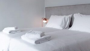 Un letto rifatto con lenzuola e cuscini bianchi, una lampada da comodino e un asciugamano piegato sul letto.