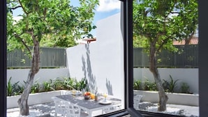Un patio con un tavolo apparecchiato per due persone, circondato da piante in vaso e con vista su una recinzione e alberi.