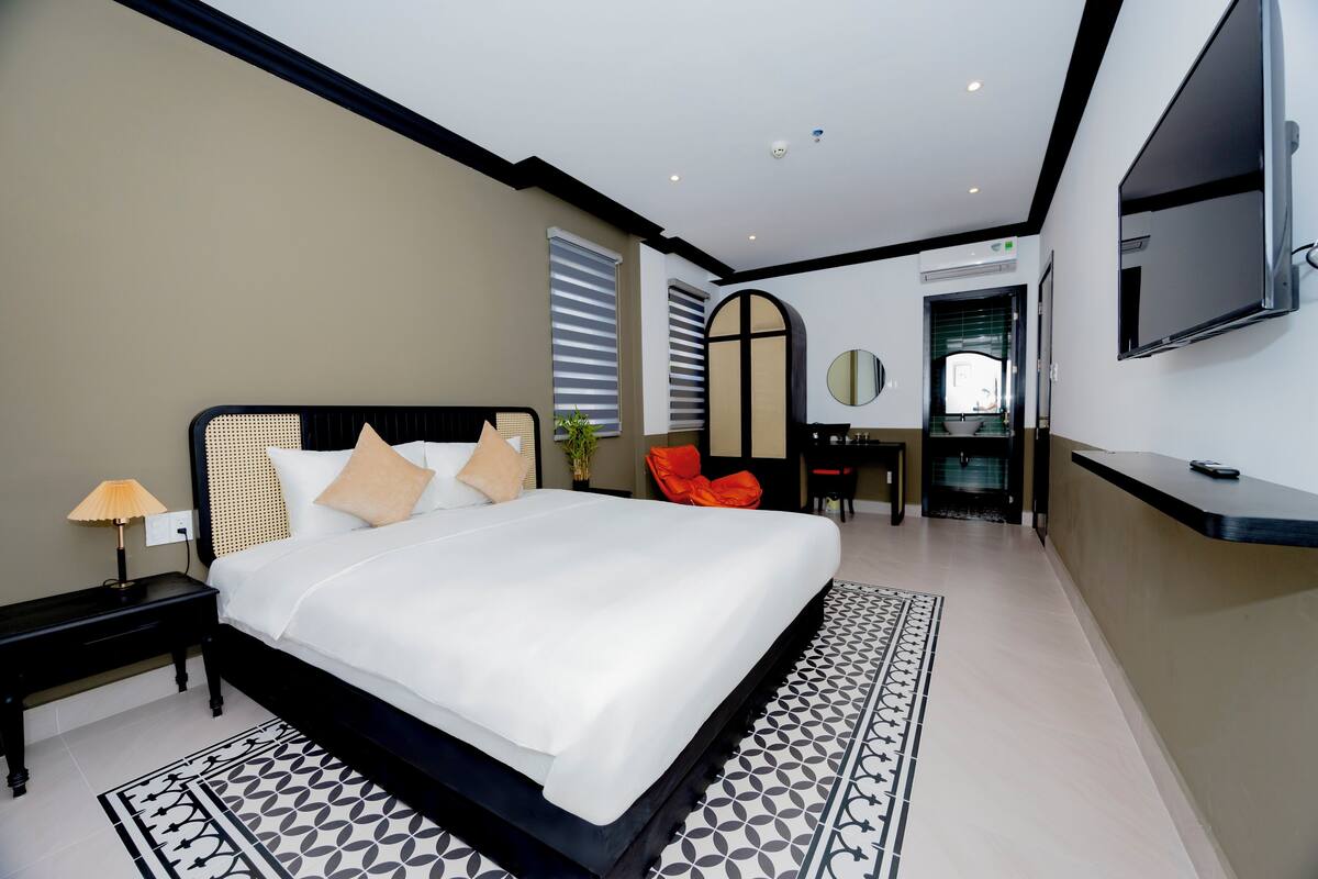A modern hotel room with a large bed, a desk, a chair, and a TV mounted on the wall.
