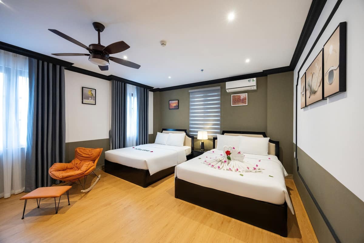 A hotel room with two beds, a ceiling fan, a window with blinds, a chair, and artwork on the walls.