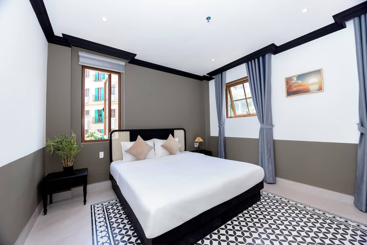 A bedroom with a large bed, a nightstand, a potted plant, and a window with curtains.