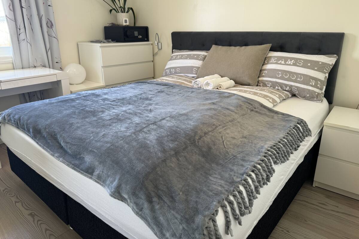 A neatly made bed with a grey blanket, a black headboard, and striped pillows.