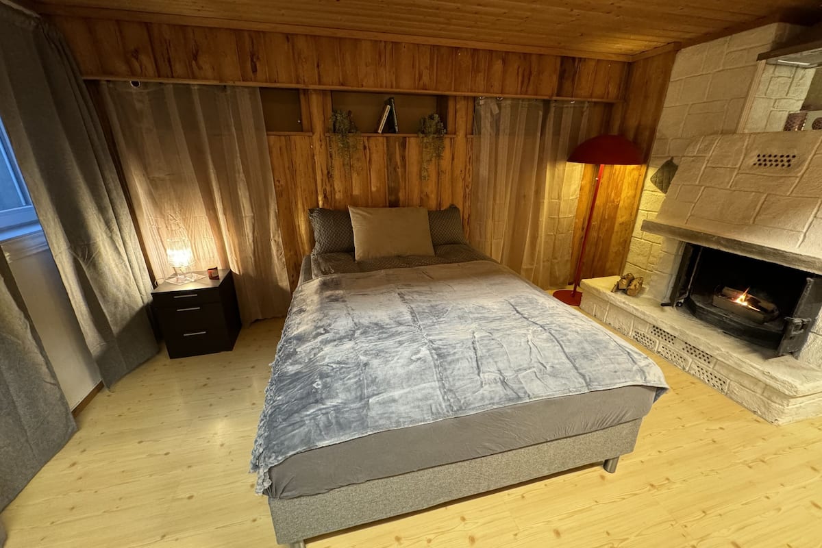 A cozy bedroom with a bed, a nightstand, a lamp, and a fireplace.