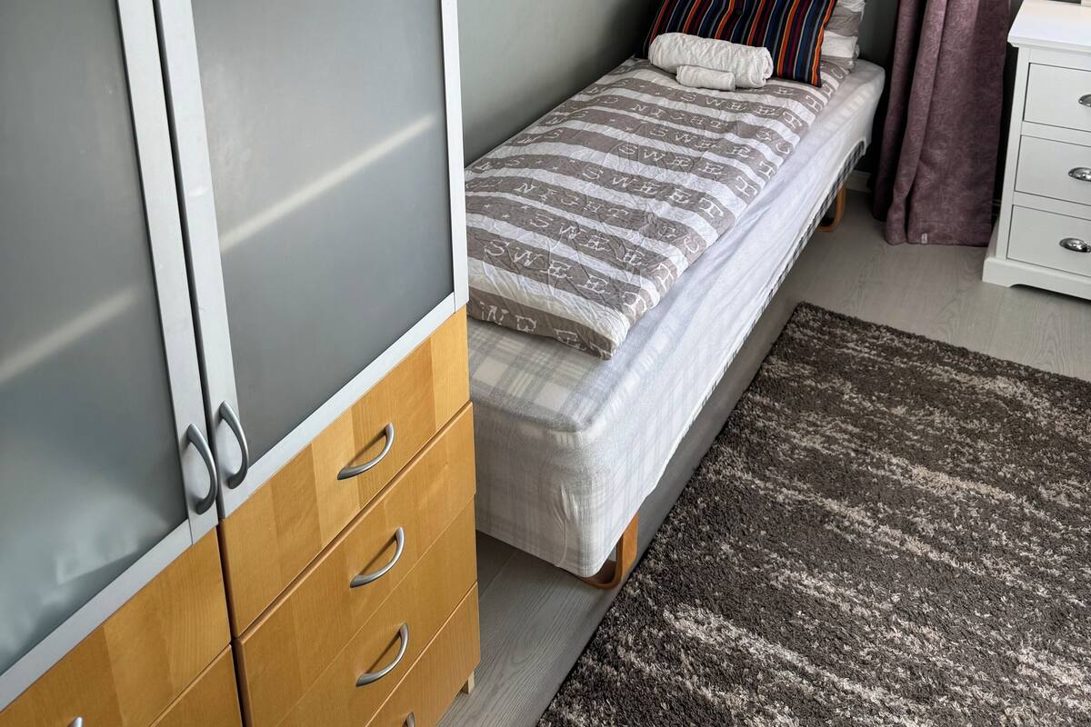 A bedroom with a bed, a wardrobe, a painting, and a window with curtains.