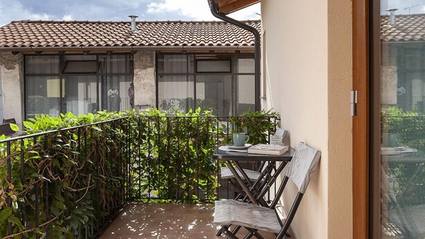 Un balcon avec une table et des chaises, un pot de fleurs et une vue sur les immeubles voisins.