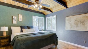 A bedroom with a bed, two windows, a ceiling fan, and a world map on the wall.