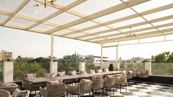 A covered outdoor seating area with a checkered floor, a long table, and wicker chairs.