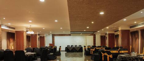 A conference room with rows of tables and chairs, a stage, and a polished floor.