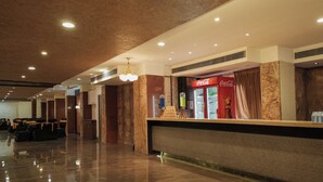 A hotel lobby with a reception desk, seating area, and a Coca-Cola refrigerator. - KANCHAN TILAK (Indore)