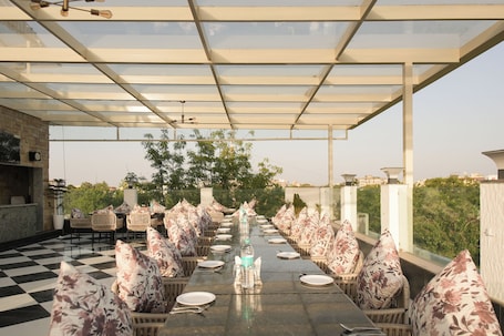 An outdoor dining area with a checkered floor, long table, and chairs with floral cushions.. KANCHAN TILAK