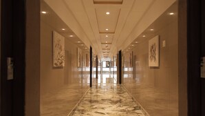 A long, well-lit hallway with marble flooring and artwork on the walls. - KANCHAN TILAK (Indore)