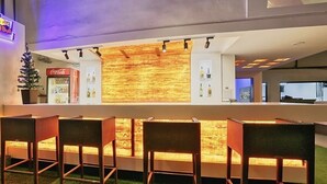 A bar area with a wooden backlit counter, seating with wicker chairs, and a Coca-Cola refrigerator. - KANCHAN TILAK (Indore)