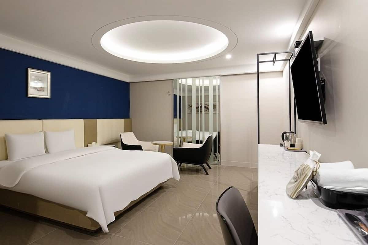 A modern hotel room with a large bed, a desk with a chair, a TV, and a bathroom area.