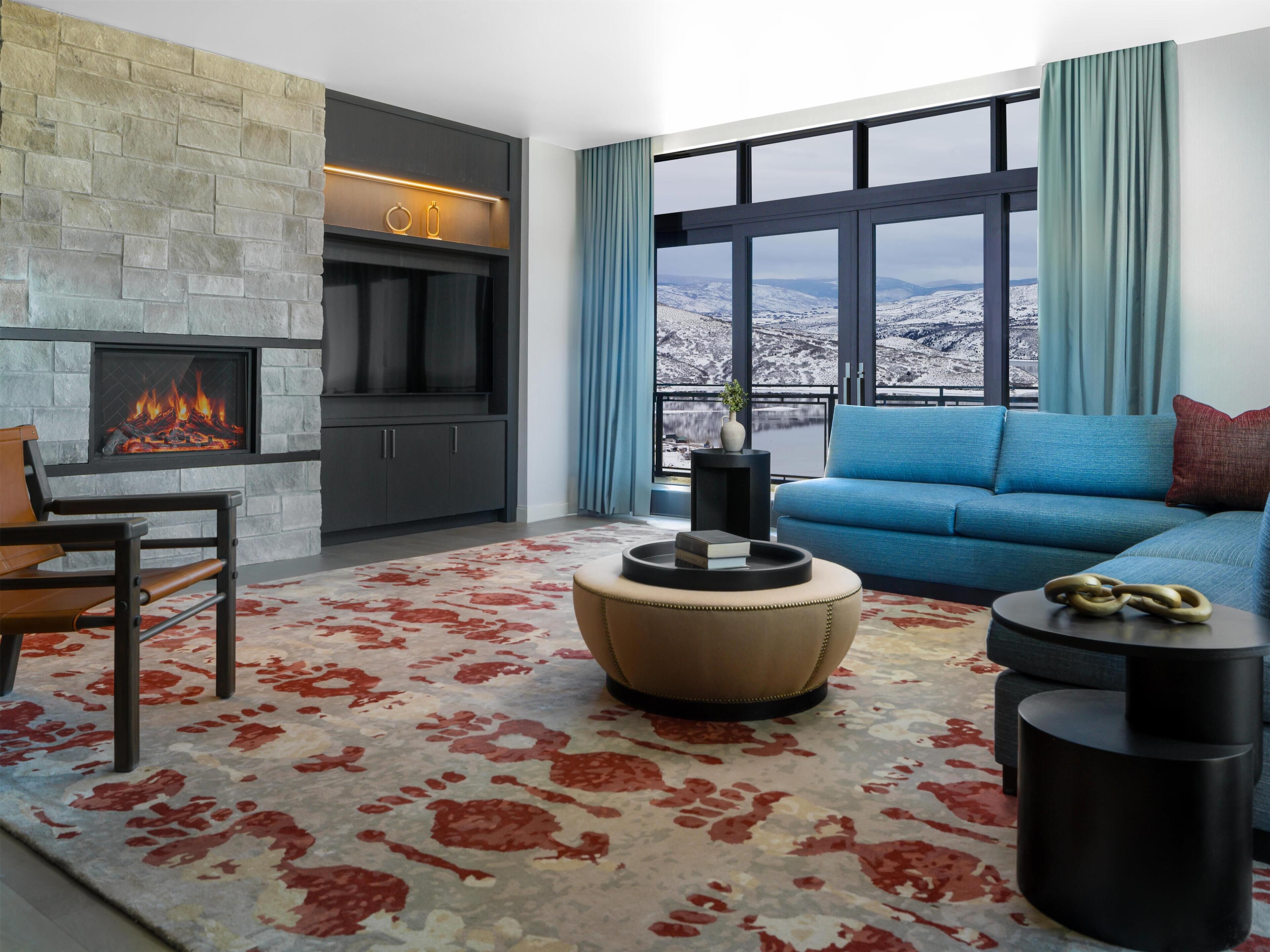 A modern living room with a fireplace, a sofa, a coffee table, and a view of a snowy landscape.
