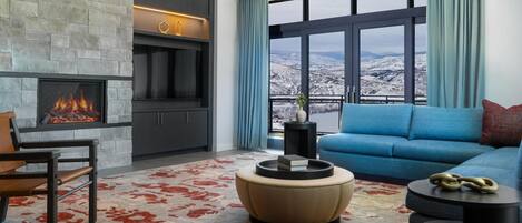 A modern living room with a fireplace, a sofa, a coffee table, and a view of a snowy landscape.