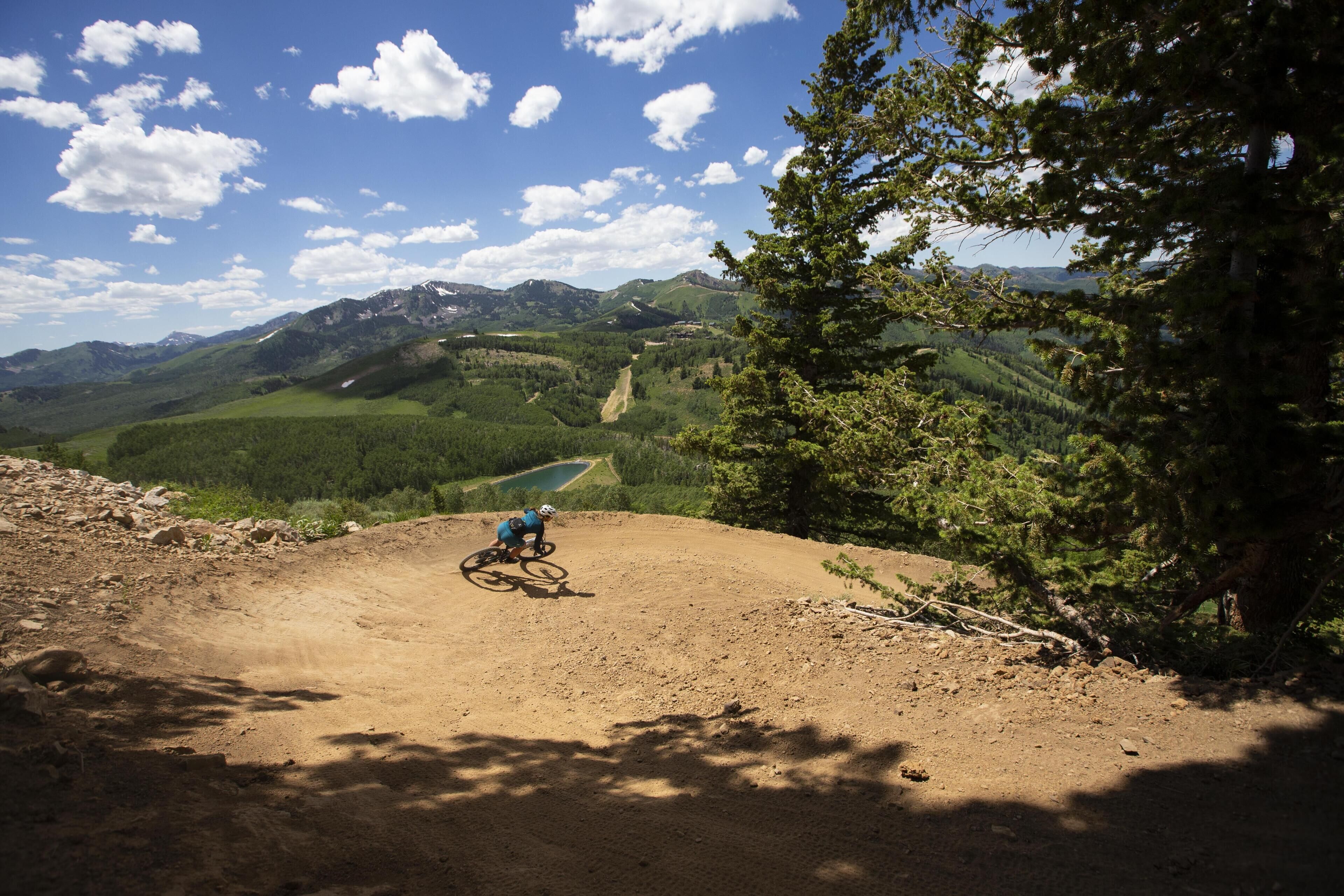 A mountain biker on a dirt trail with a view of green hills and mountains in the background.