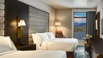Een hotelkamer met twee bedden, een bureau, een stoel, een lamp, een televisie en een groot raam met uitzicht.