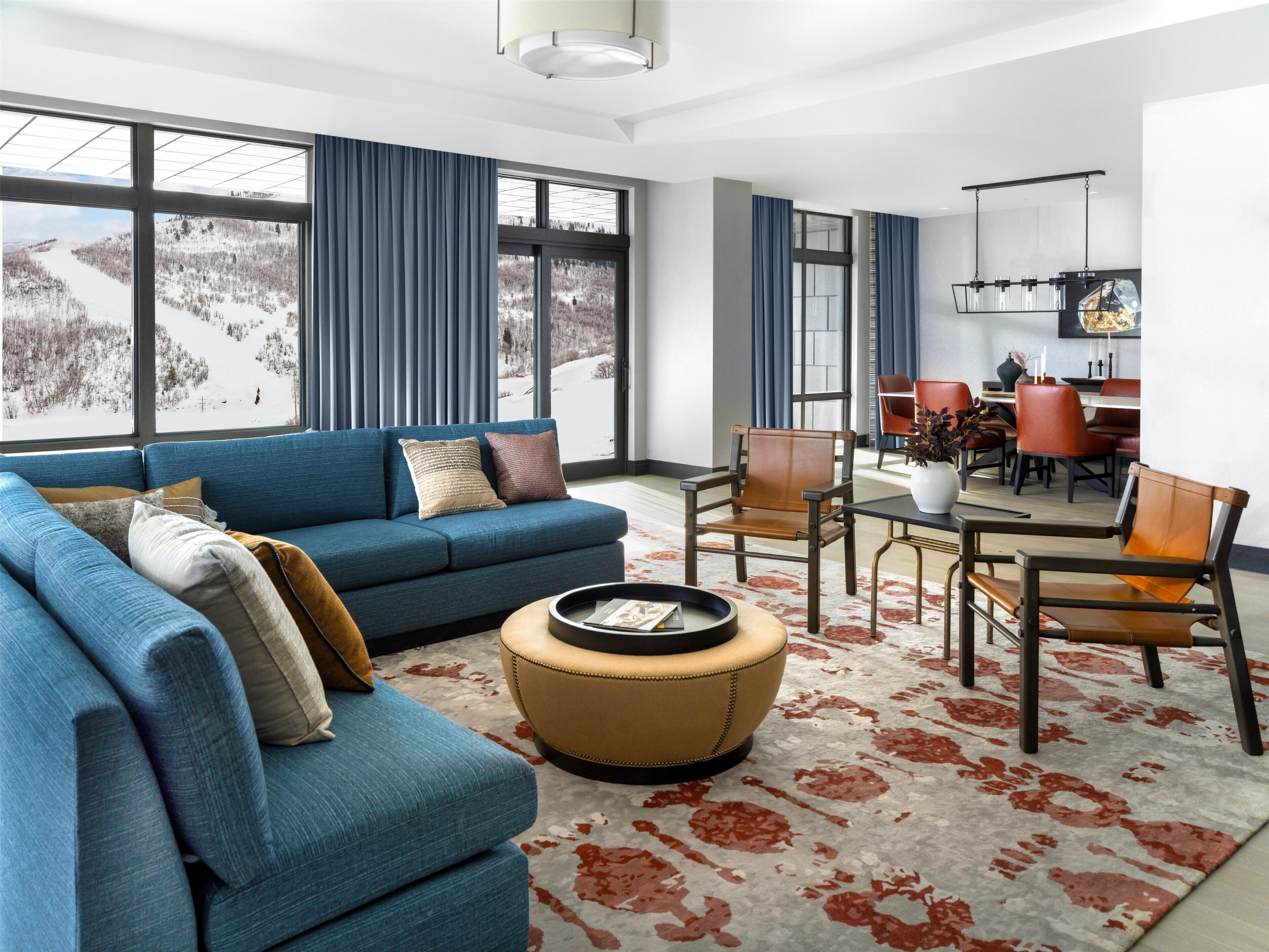 Un salon moderne avec un canapé bleu, un pouf rond et un coin repas avec des chaises rouges.