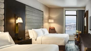 Habitación de hotel con dos camas, un escritorio, una silla, una lámpara y un ventanal con vistas.