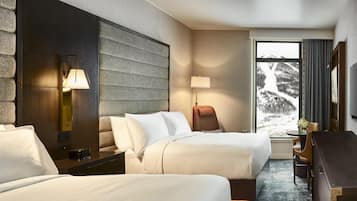 Habitación de hotel con dos camas, un escritorio, una silla, una lámpara, un televisor y una ventana con vista a la montaña.