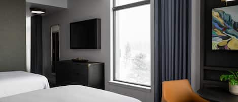 Habitación de hotel con dos camas, un escritorio, una silla, un televisor y un ventanal grande.