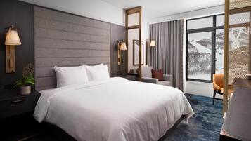 A modern hotel room with a large bed, bedside lamps, a chair, and a view of a snowy landscape.