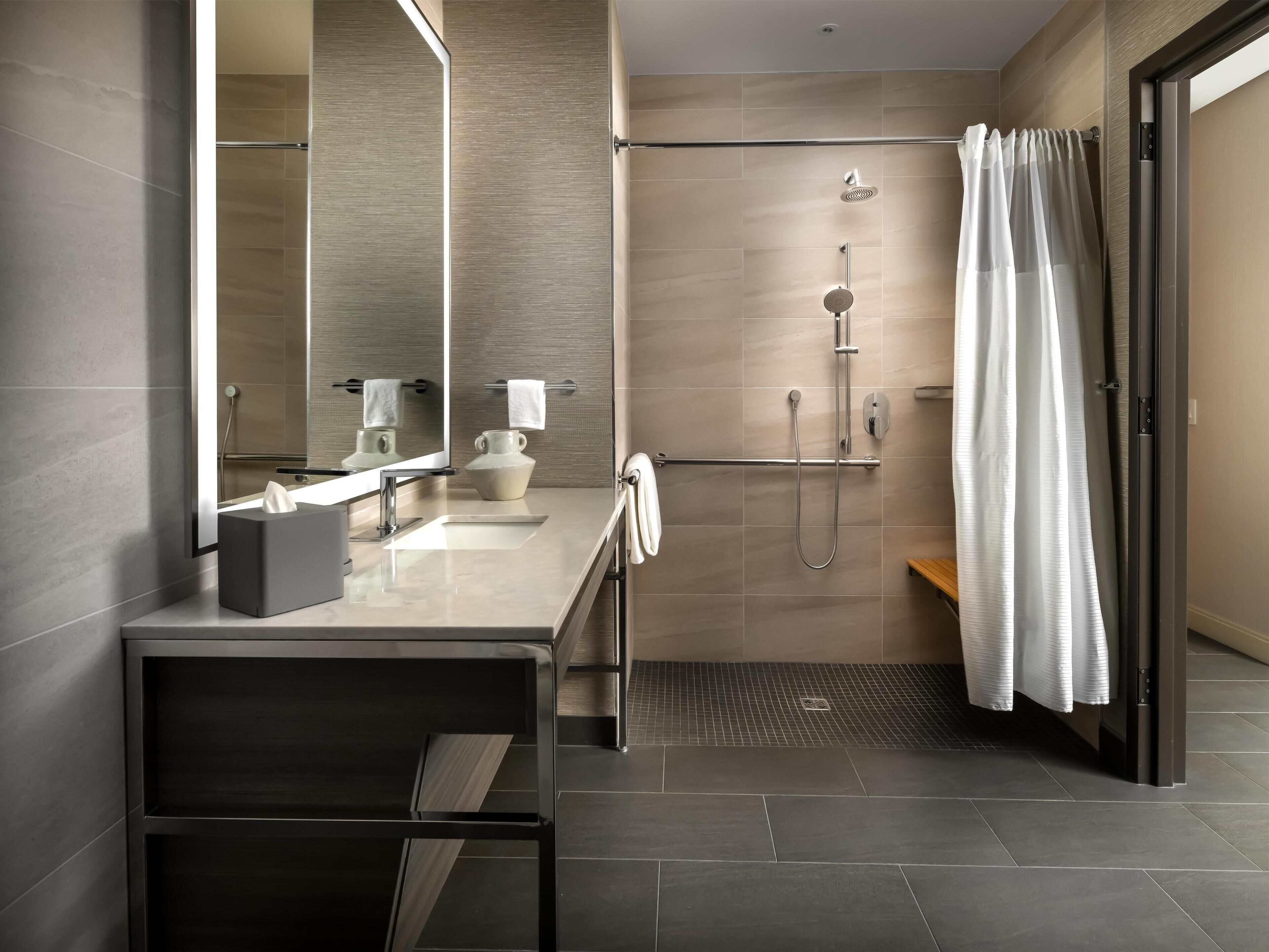Ein modernes Badezimmer mit Dusche, Waschtisch mit Spiegel und Handtuchhalter.
