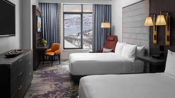 Habitación de hotel con dos camas, un escritorio, una silla, un televisor, un ventanal con vistas a un paisaje nevado y dos lámparas de pared.