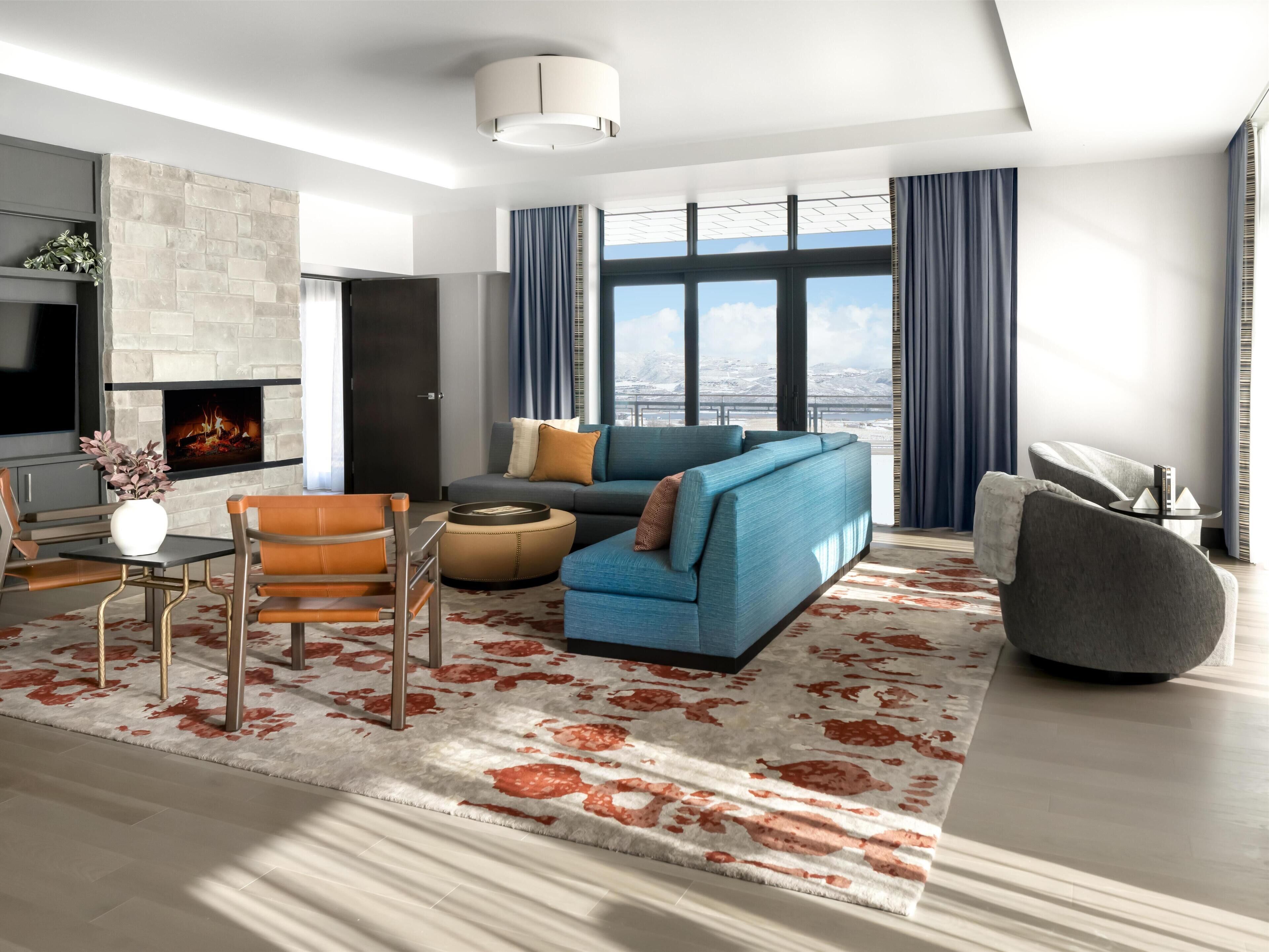 Ein modernes Wohnzimmer mit Kamin, Sofa, Sessel und einem großen Fenster mit Vorhängen.