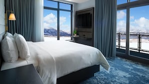 Quarto de hotel com uma cama grande, televisão e varanda com vista para as montanhas.