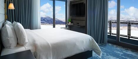 A hotel room with a large bed, a TV, and a balcony with a mountain view.