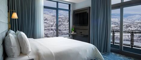Een hotelkamer met een groot bed, een televisie, een bureau en uitzicht op een besneeuwd landschap.