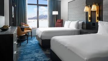 Habitación de hotel con dos camas, un escritorio, una silla, una lámpara y vistas a un paisaje nevado.