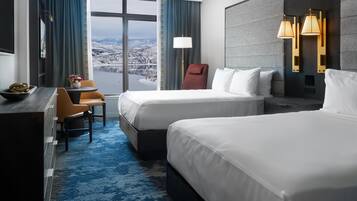 Habitación de hotel con dos camas, un escritorio, una silla, una lámpara y vistas a un paisaje nevado.