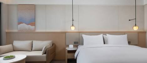 Une chambre d’hôtel moderne avec un grand lit, un canapé, une petite table et deux lampes suspendues.