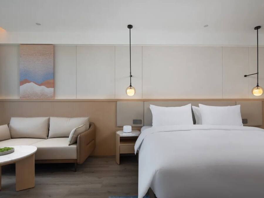 Una habitación de hotel moderna con una cama grande, un sofá, una mesita y dos lámparas colgantes.
