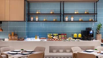 Een modern restaurant met blauwe betegelde muren, een buffet met diverse gerechten en een koffieapparaat.