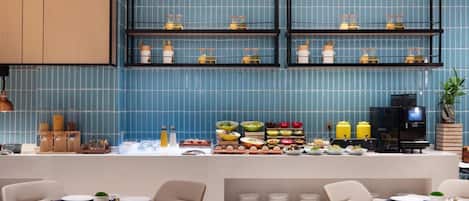 A modern restaurant with blue tiled walls, a buffet counter with various dishes, and a coffee machine.