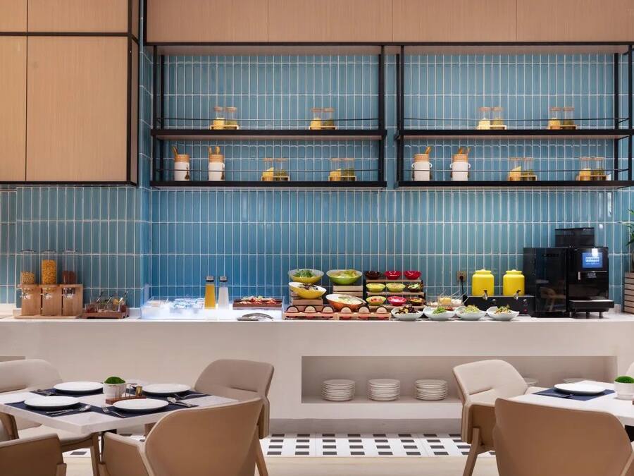 Een modern restaurant met blauwe betegelde muren, een buffet met diverse gerechten en een koffieapparaat.