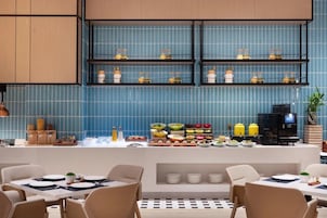 Un restaurante moderno con paredes de azulejos azules, una barra de buffet con diferentes platos y una máquina de café.
