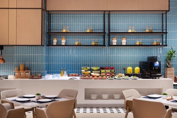 A modern restaurant with blue tiled walls, a buffet counter with various dishes, and a coffee machine.