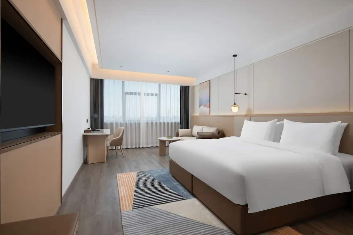 A modern hotel room with a large bed, a desk, a chair, and a TV.