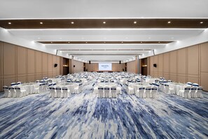 A large conference room with rows of tables and chairs, a stage with a screen, and a 'NOVOTEL' sign. - Novotel Jiaxing Port Area (Jiaxing)