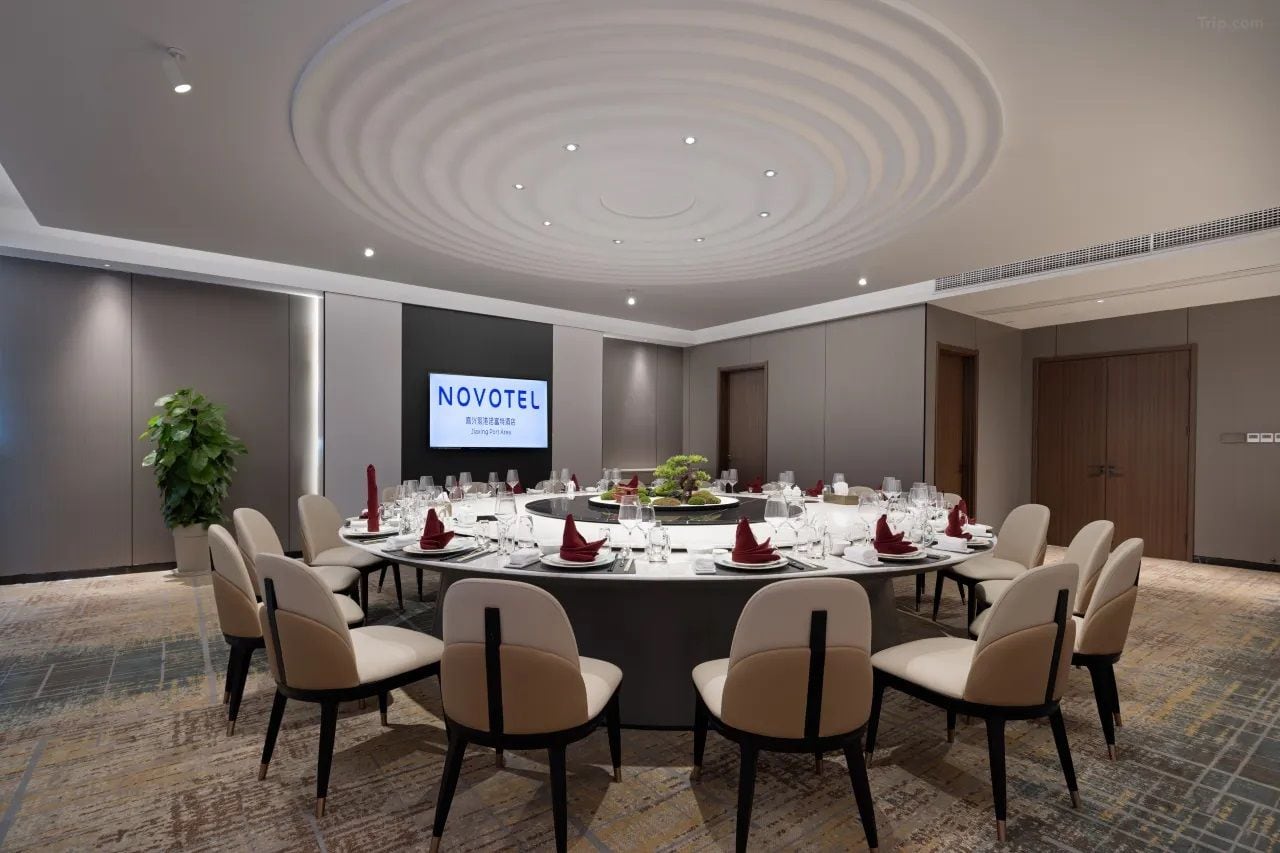 A conference room with a round table, beige chairs, and a projector screen displaying 'NOVOTEL'.