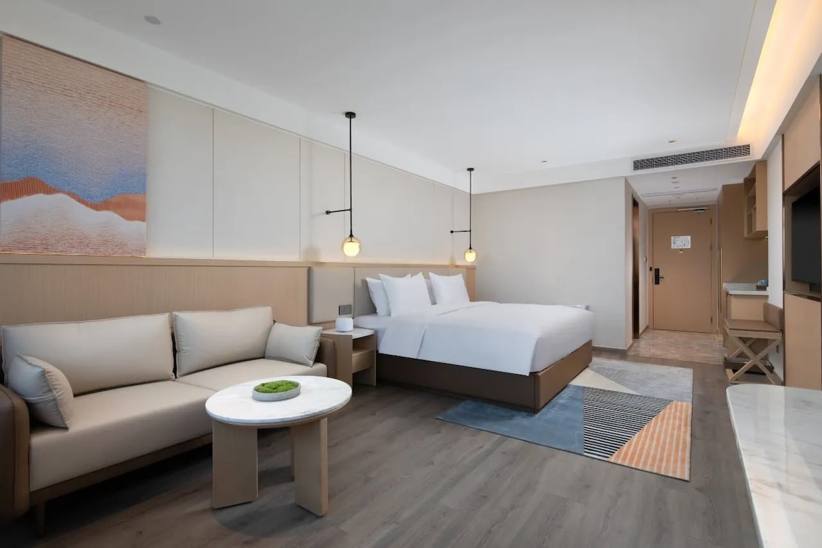 A modern hotel room with a bed, a sofa, a small table, and a TV.