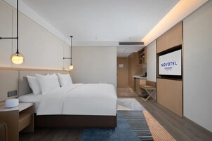 Una habitación de hotel moderna con una cama grande, mesitas de noche, un televisor y vistas al pasillo.