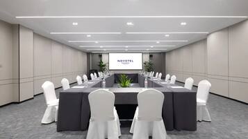 Un salón de conferencias con una larga mesa, sillas blancas y una pantalla que muestra "NOVOTEL".