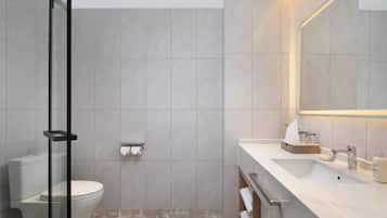 Un baño moderno con cabina de ducha de vidrio, inodoro, lavamanos con espejo y toallero.