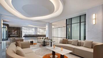 A modern hotel lobby with a curved ceiling, large windows, and a seating area with sofas and tables.