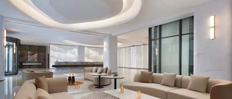 A modern hotel lobby with a curved ceiling, large windows, and a seating area with sofas and tables.
